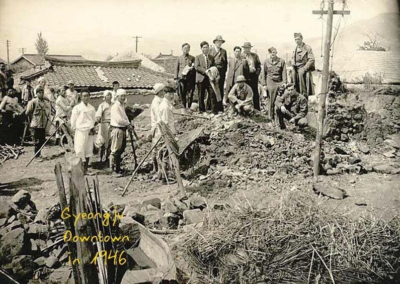 A group of men in 1946, standing and working in a rural setting with traditional buildings and a wooden structure. 2