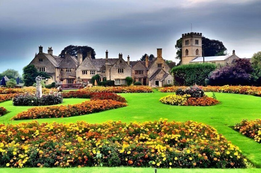 A historic building with a tower, surrounded by manicured gardens and a variety of colorful flowers. 1