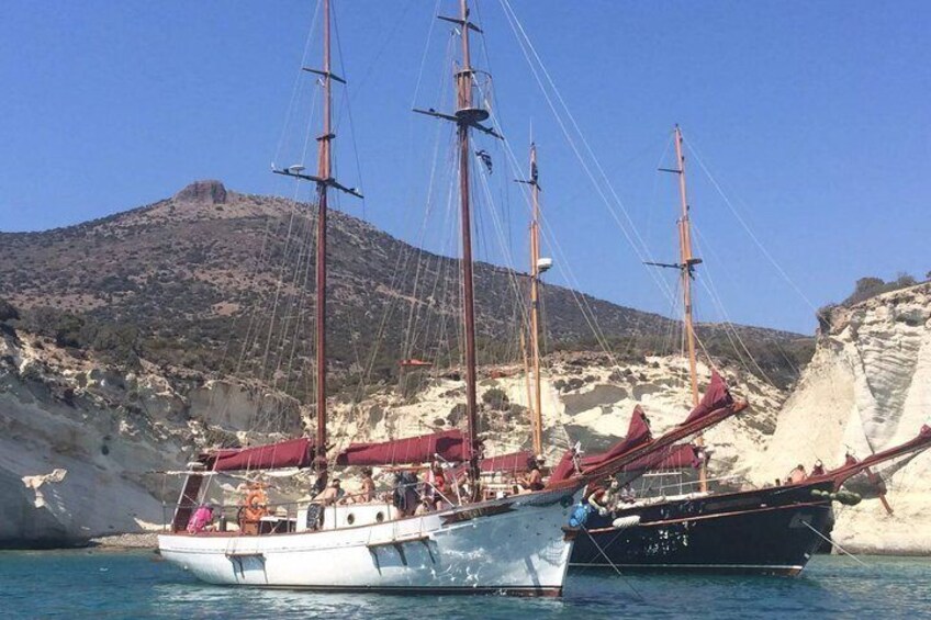 A sailing boat with multiple masts and sails, docked near a rocky coastline with a mountain in the background. 5