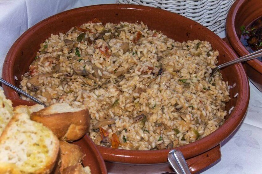 A large clay pot filled with rice and vegetables, accompanied by slices of bread. 3