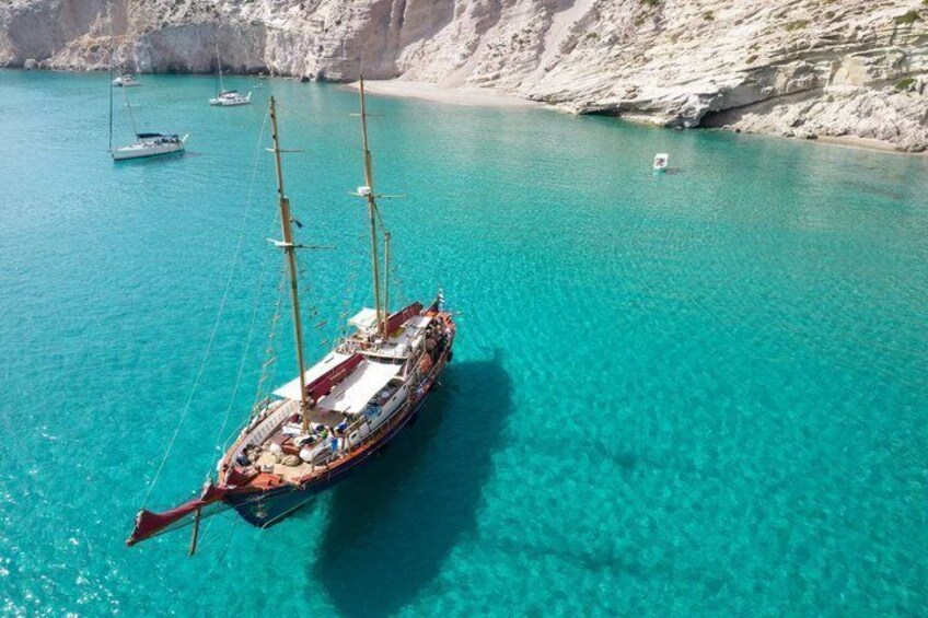 A sailboat on turquoise water near a rocky coastline. 1
