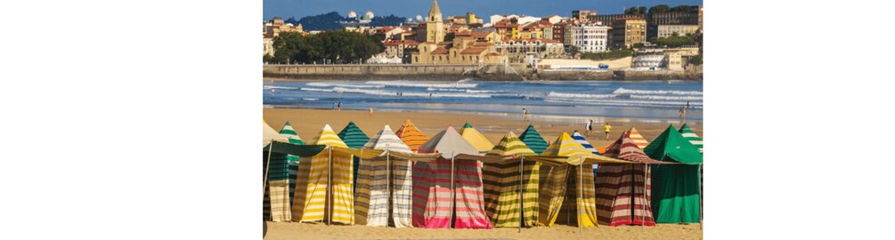 A beach with colorful striped beach umbrellas and a historic town in the background. 1