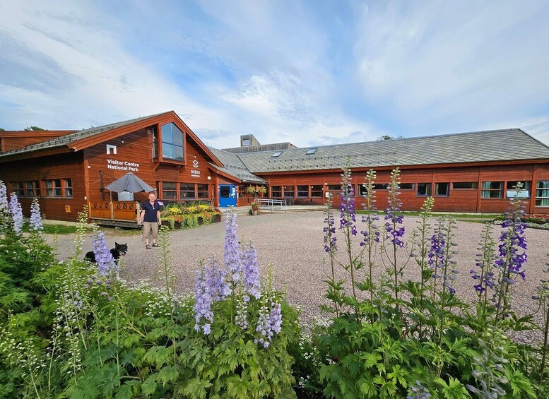 A wooden visitor center with a gravel courtyard and purple flowers. 1