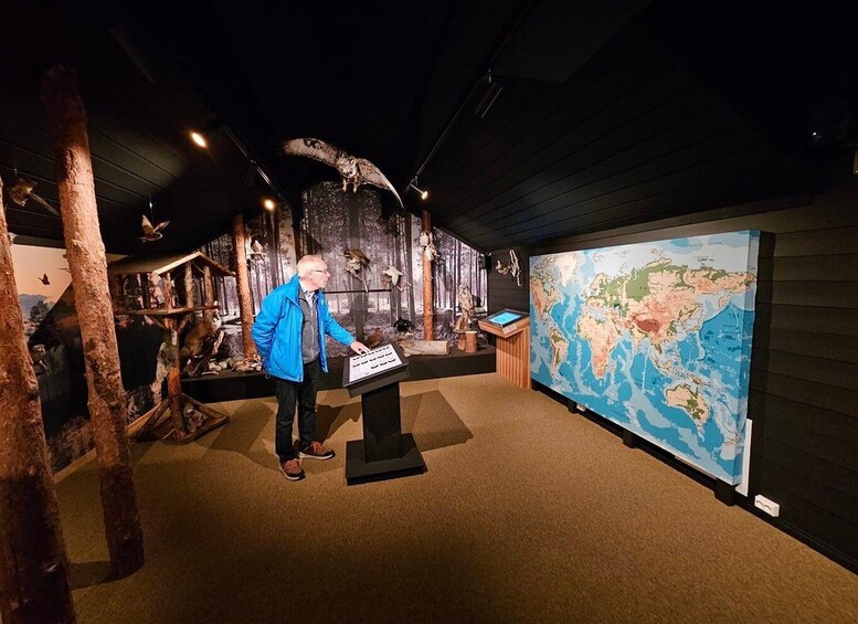 A museum exhibit with a large world map, a man presenting, and various animal taxidermy. 3