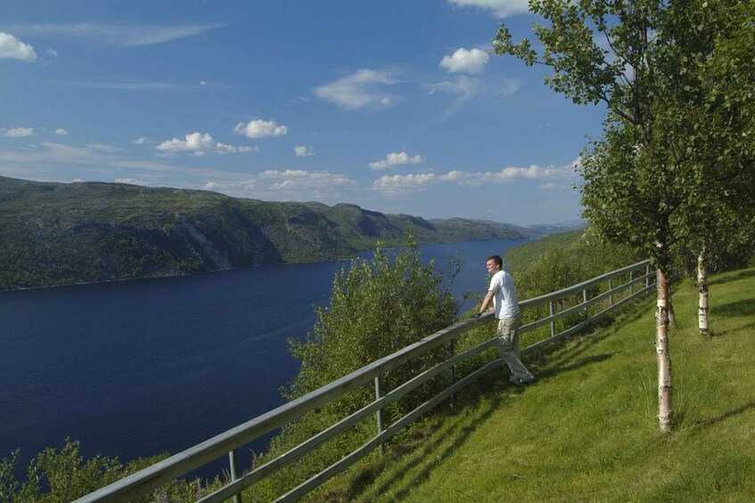 A person walking along a metal railing overlooking a lake with hills in the distance. 5