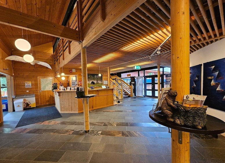 A wooden interior with a reception desk, a staircase, and a bear statue. 2