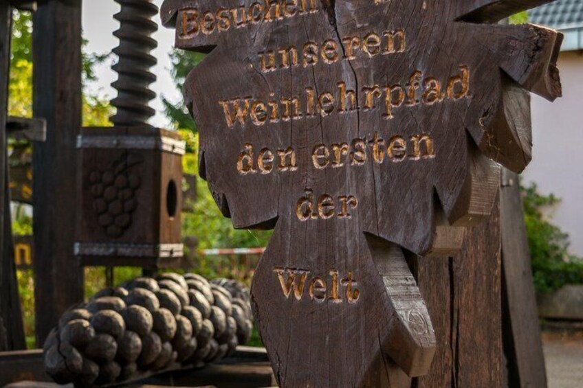 A wooden sign with carved text, a wooden structure, and a pine cone in the background. 3