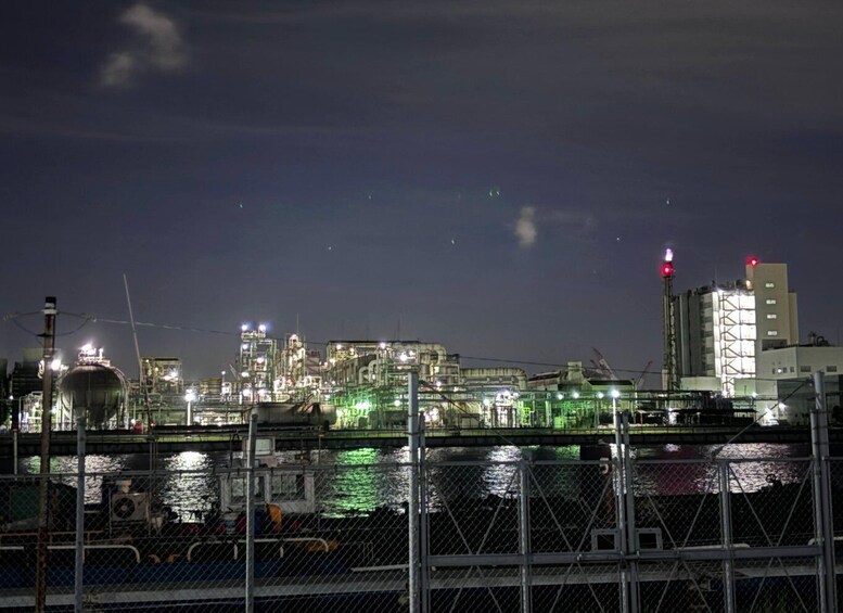 A nighttime industrial area with illuminated structures and a body of water in the foreground. 2