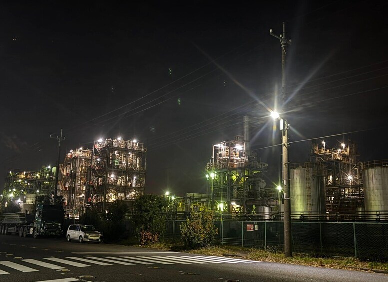 A nighttime industrial complex with illuminated structures and a road with vehicles. 4