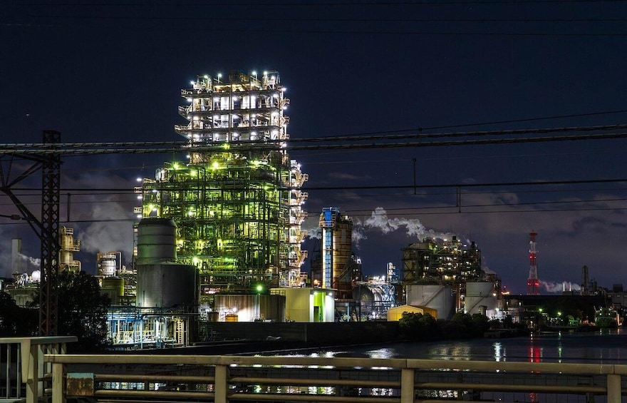 A large industrial complex at night with multiple illuminated structures and a body of water in the foreground. 2