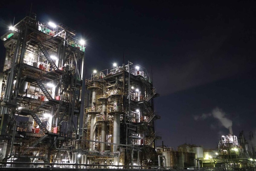 An industrial complex at night with multiple illuminated structures and smokestacks emitting smoke. 3