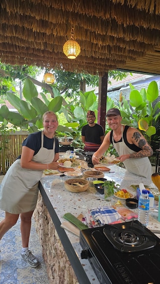 Two people serving food at an outdoor dining area with a thatched roof, surrounded by lush greenery. 2