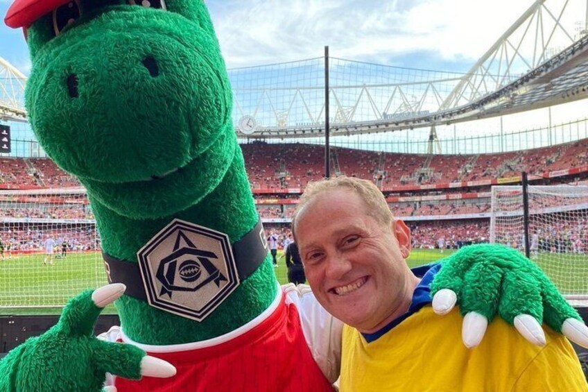 A person with a green mascot in a stadium. 1