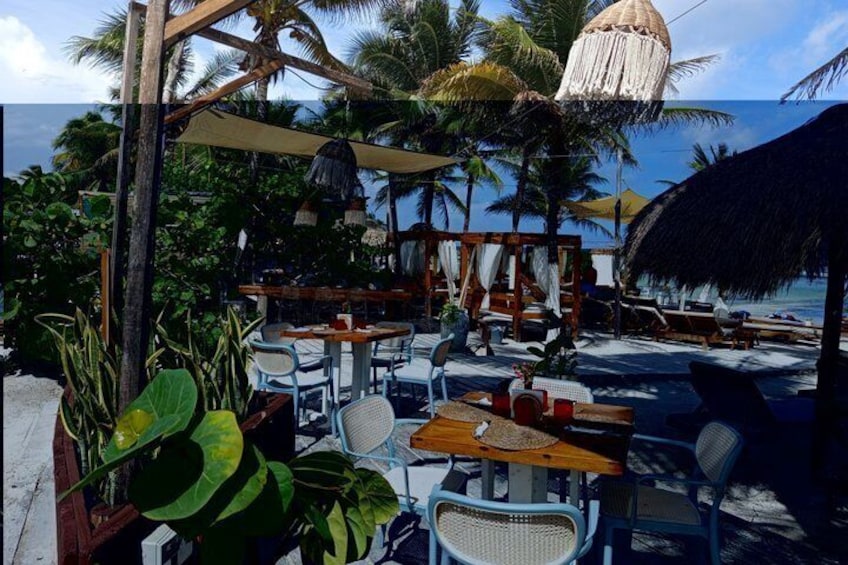 A beachside café with outdoor seating, palm trees, and a thatched roof. 5
