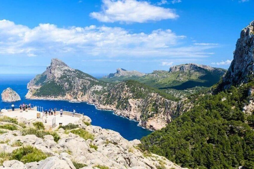 A coastal landscape with rocky cliffs, a clear blue sea, and a group of people on a viewing platform. 2