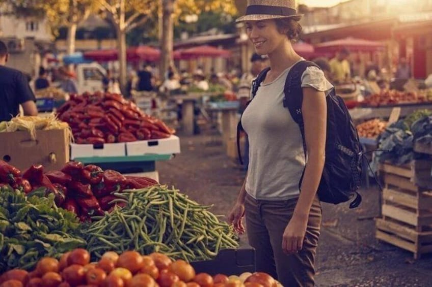 A person standing at an outdoor market with various vegetables on display. 4