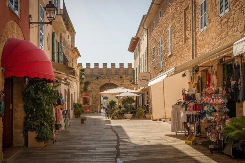 A narrow street with shops, a red umbrella, and a stone archway. 3