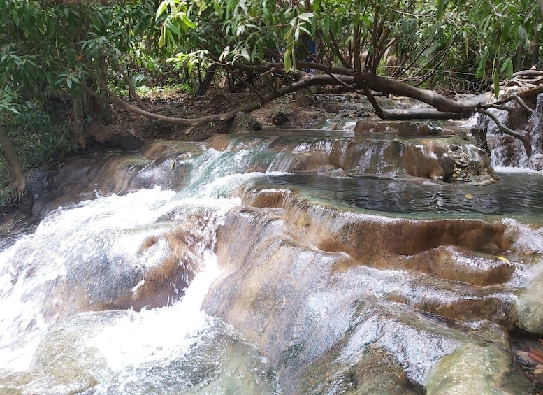 A natural waterfall cascading over terraced rock formations surrounded by dense foliage. 3