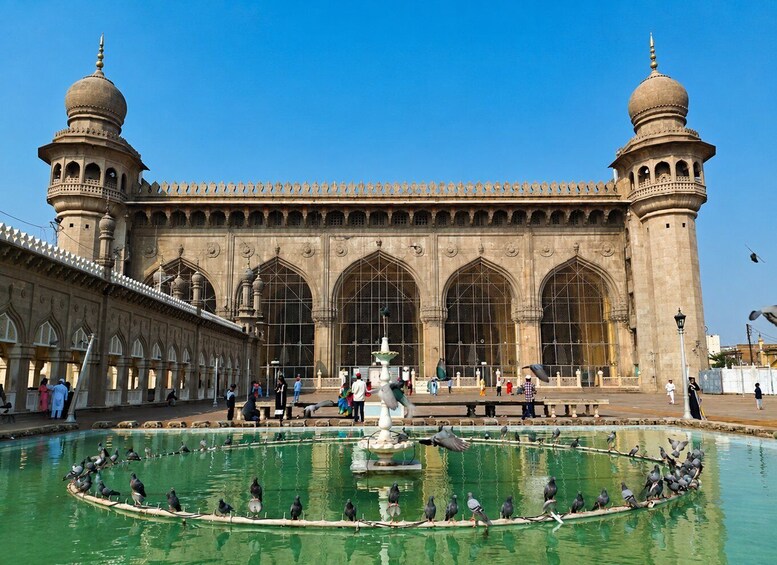 A historic building with arched windows and domed towers, surrounded by a large fountain with birds. 4