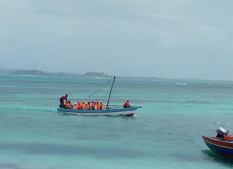 A small boat with people wearing orange life jackets on calm turquoise waters. 4