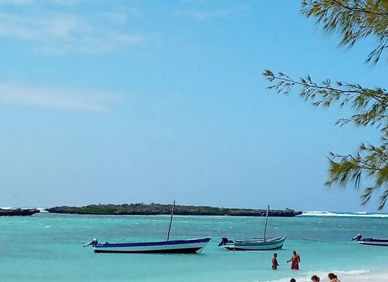 A beach with several boats anchored in the water, people walking along the shore, and a clear sky. 5