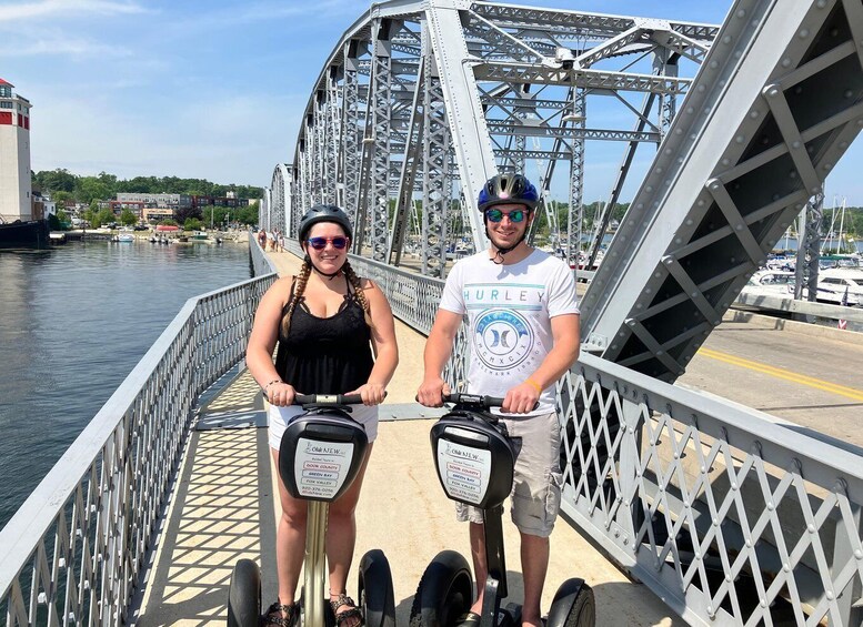 Two people on a bridge with a river and buildings in the background. 1