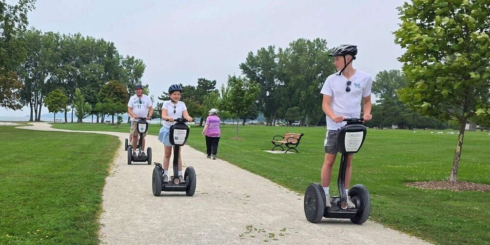 People riding segways on a path in a park with trees and a bench. 2