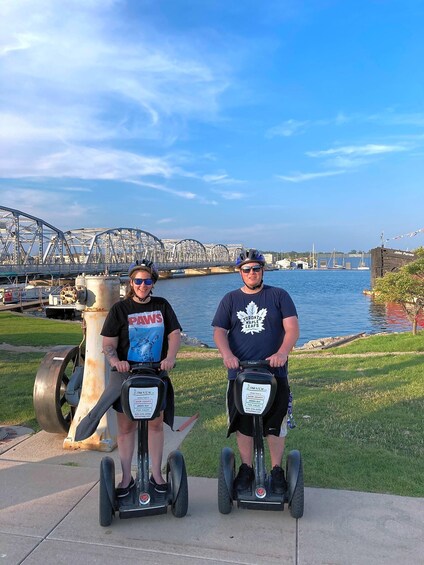 Two people on segways by a waterfront with a bridge in the background. 4