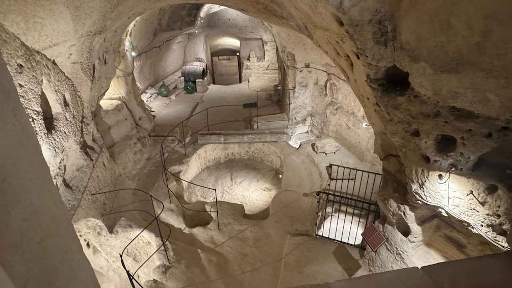 An underground chamber with stone walls, a central opening, and a metal railing. 2