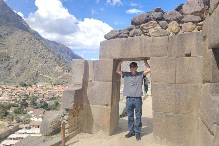 A person standing in front of a stone structure with a mountainous landscape in the background. 4