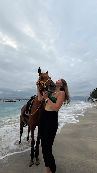 A person with a horse on a beach with boats in the background. 2