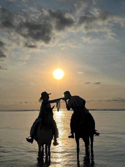 Two people on horseback silhouetted against a sunset, with the sun low on the horizon. 4