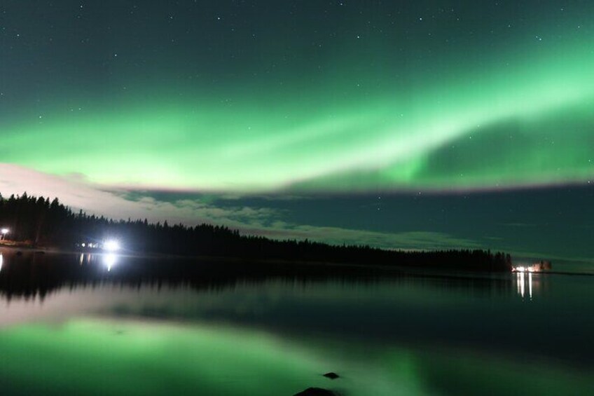 A night scene with the Northern Lights over a calm lake, reflecting lights from a distant shoreline. 3