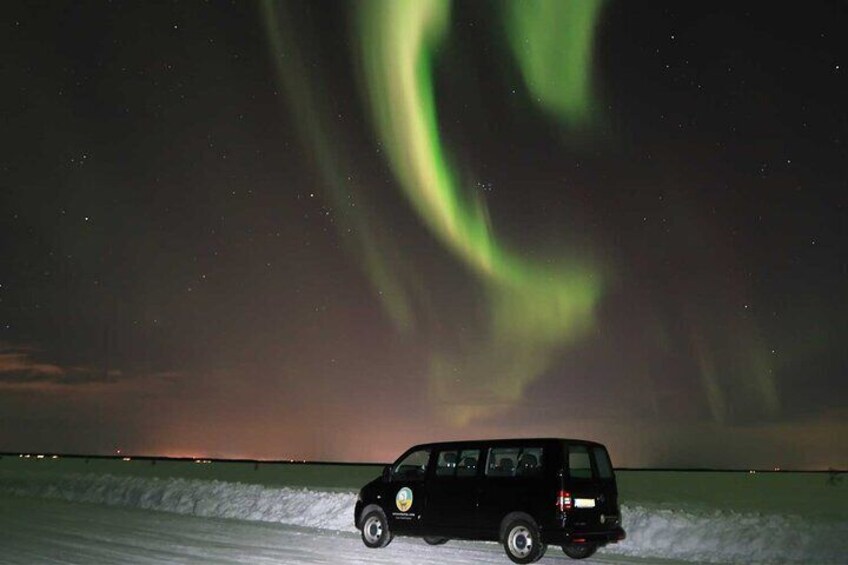 A vehicle on a snowy road with the Northern Lights in the background. 2
