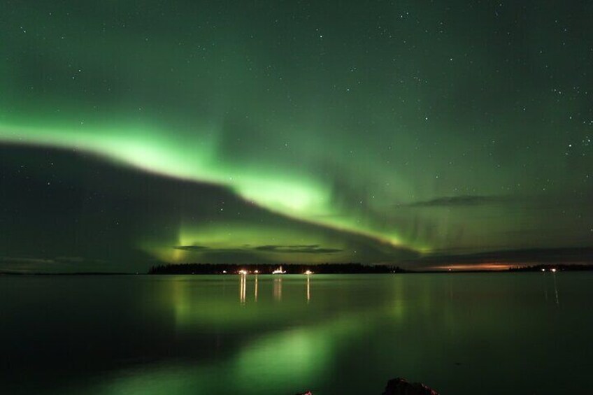 The Northern Lights over a calm body of water with reflections of lights on the surface. 4
