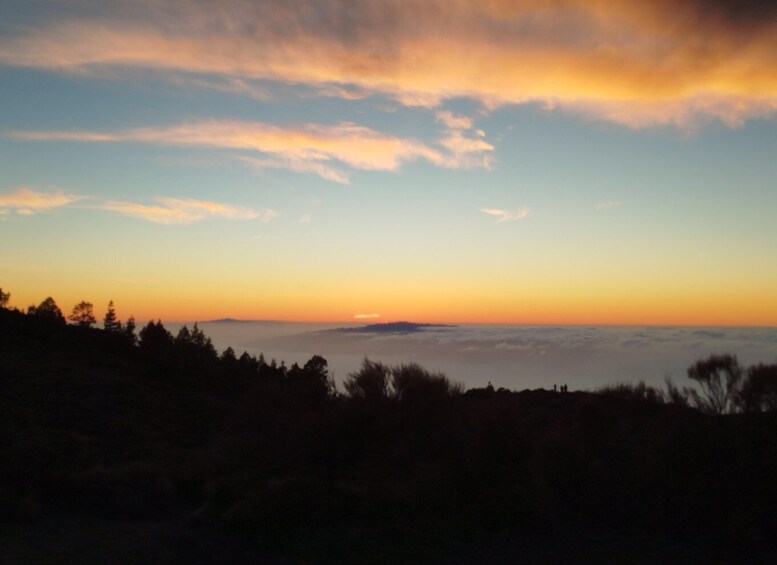 A sunset over a mountainous landscape with silhouettes of trees and a clear sky. 4