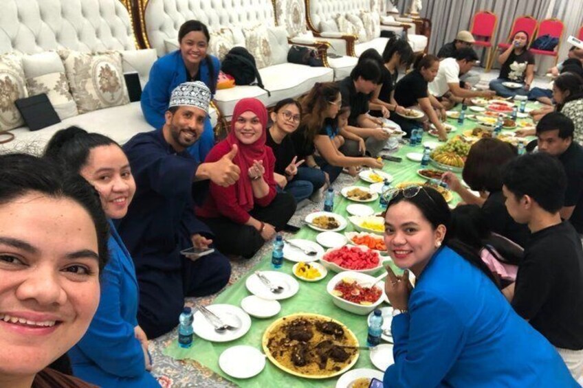 A group of people sitting on the floor around a table with various dishes. 1