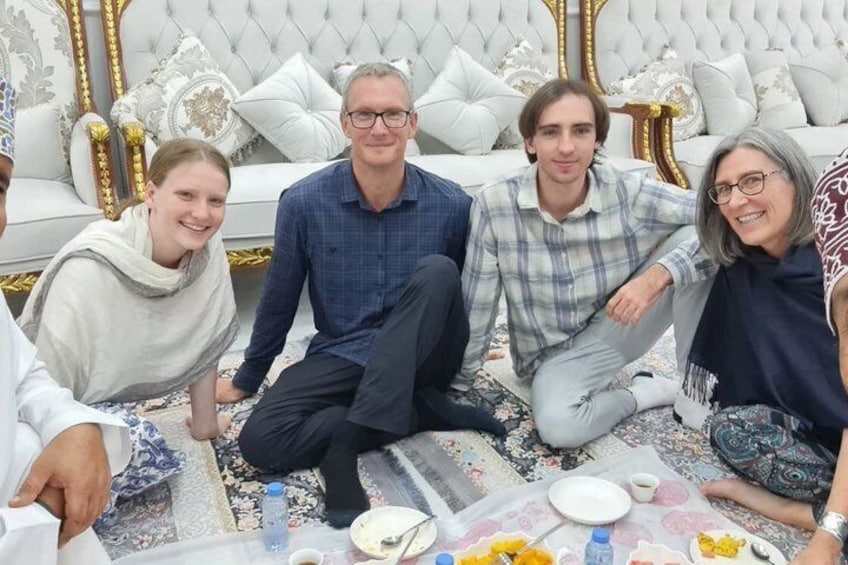 A group of people sitting on a patterned rug in a room with a white sofa and decorative pillows. 4