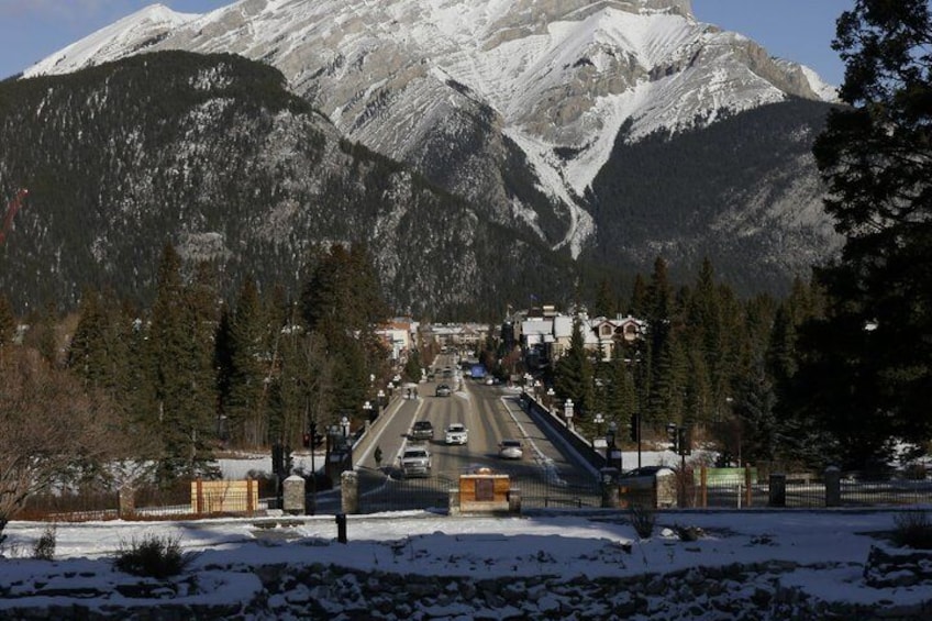 A snow-covered road with vehicles, a mountain range, and a town in the background. 5