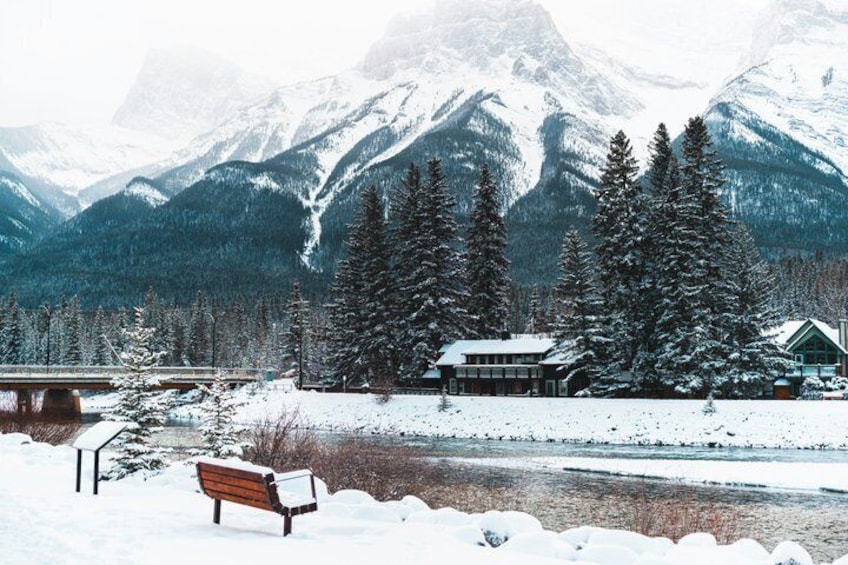 A snow-covered landscape with a wooden bench, a cabin, and snow-laden trees in the background. 4