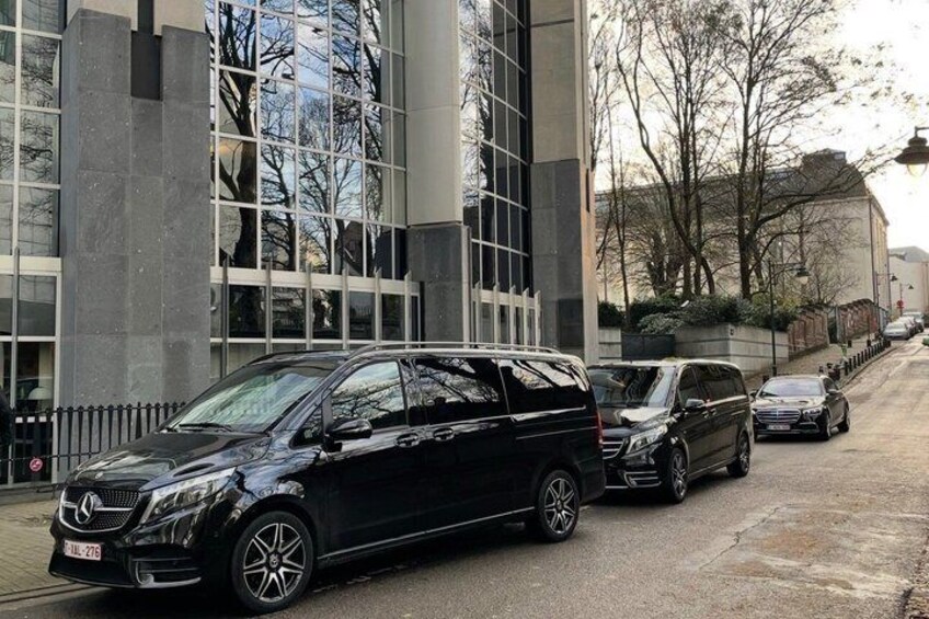 A black Mercedes-Benz SUV parked on a city street with modern buildings and trees in the background. 2