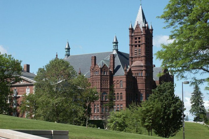 A large, historic red brick building with multiple towers and spires, surrounded by lush green trees and a well-maintained lawn. 4