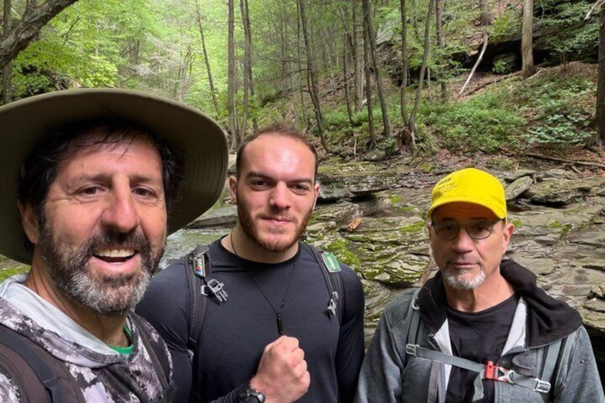 Three people in a forested area with a stream. 1