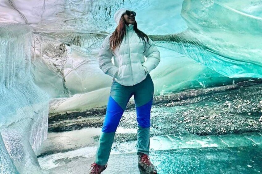 A person standing inside an ice cave with visible ice formations and a water stream at the bottom. 3