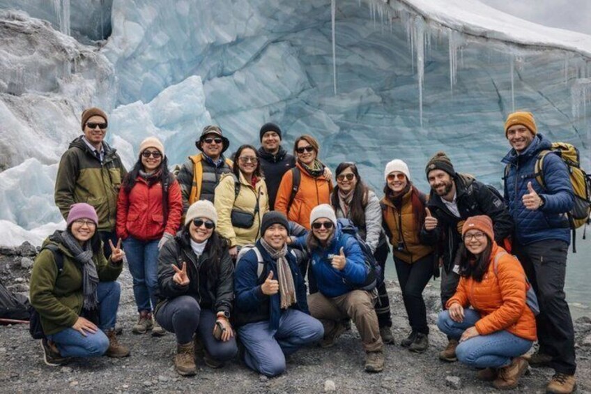 A group of people in outdoor winter clothing posing in front of a glacier. 5