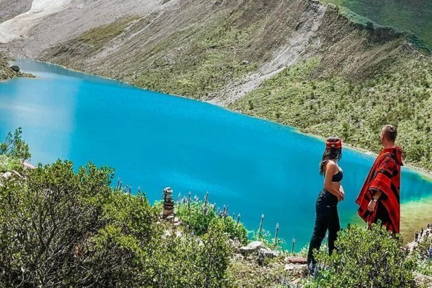 A turquoise lake surrounded by mountains, with a person in a red cloak standing on a cliff. 4