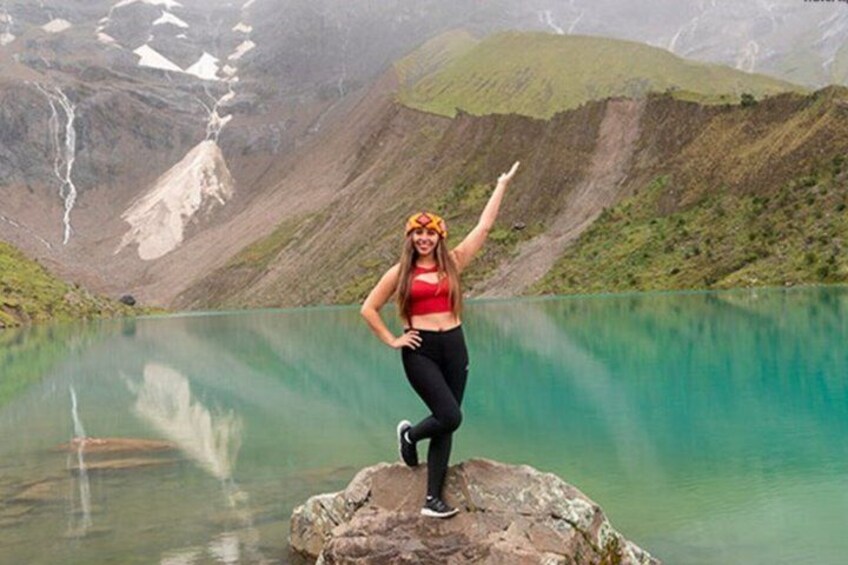 A person standing on a rock by a turquoise lake with mountains in the background. 2