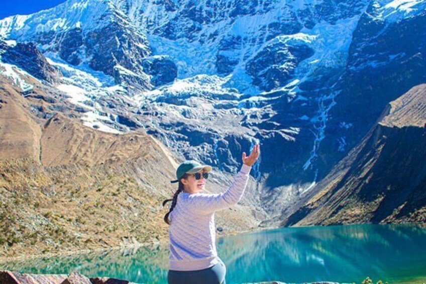 A person standing by a turquoise lake with snow-capped mountains in the background. 3