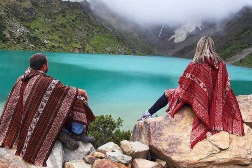 Two people sitting on rocks overlooking a turquoise lake with mountains in the background. 5