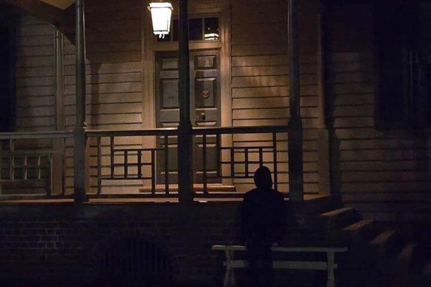 A wooden building with a porch, a person sitting on a bench, and a street lamp. 5